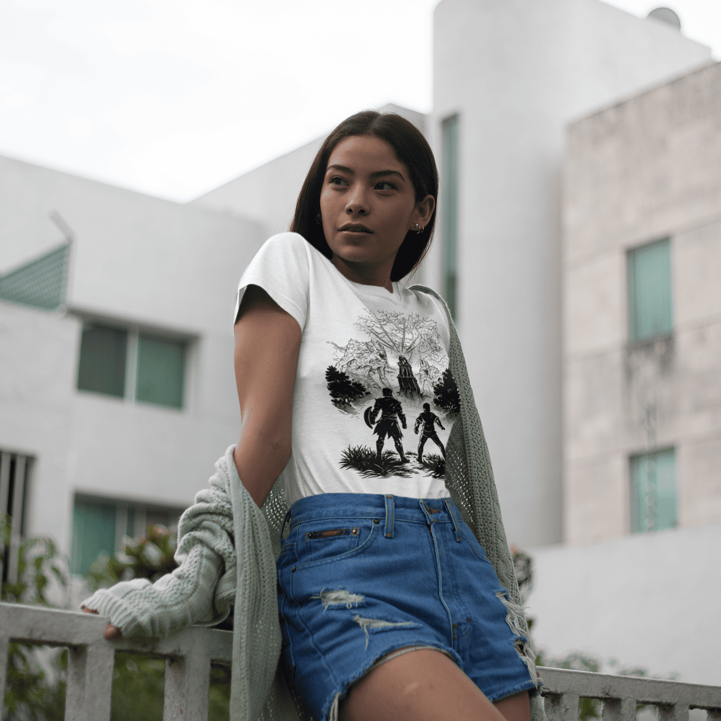 Woman wearing a graphic t-shirt and denim shorts standing outdoors with a building in the background