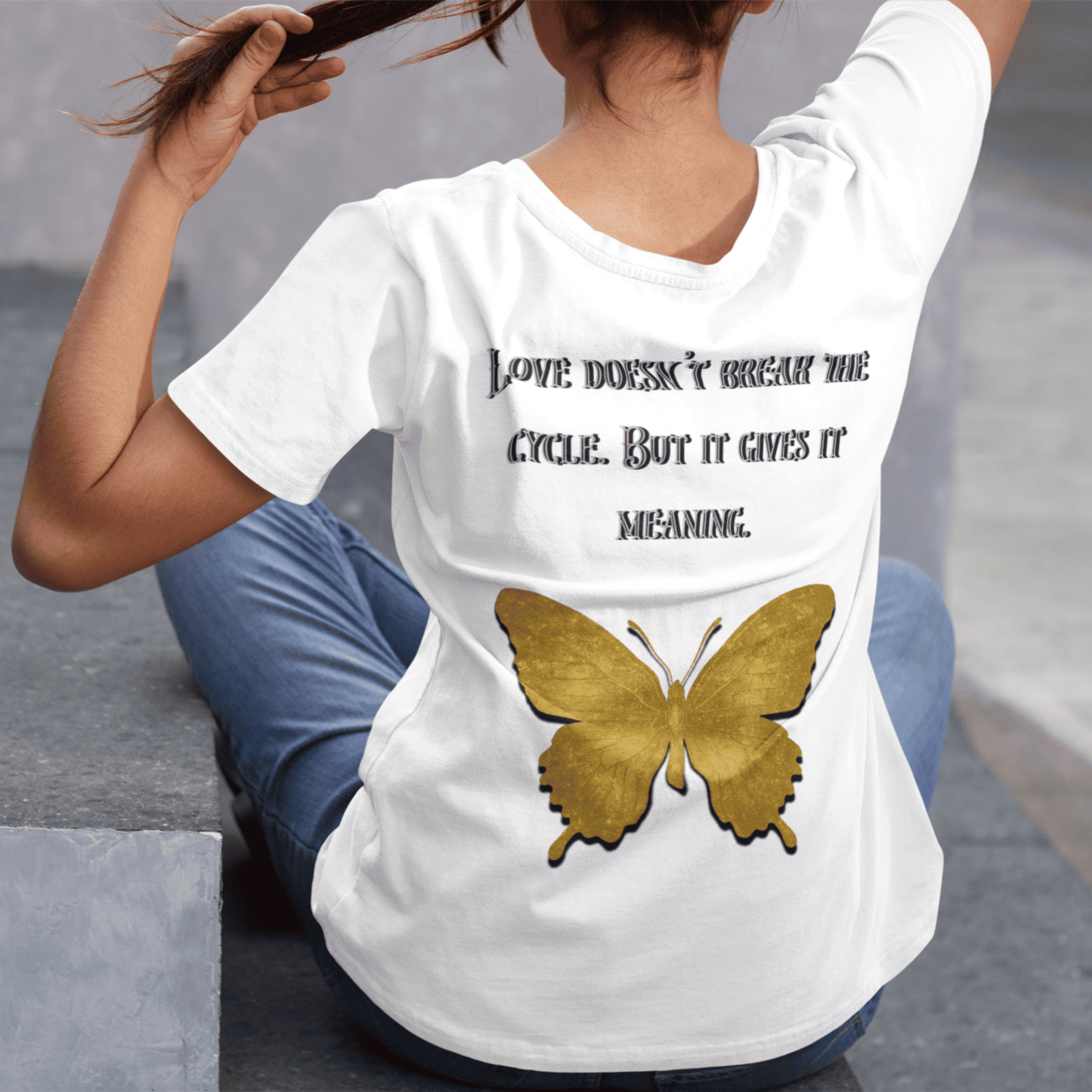 Person wearing a white t-shirt with a butterfly design and text, sitting on steps.