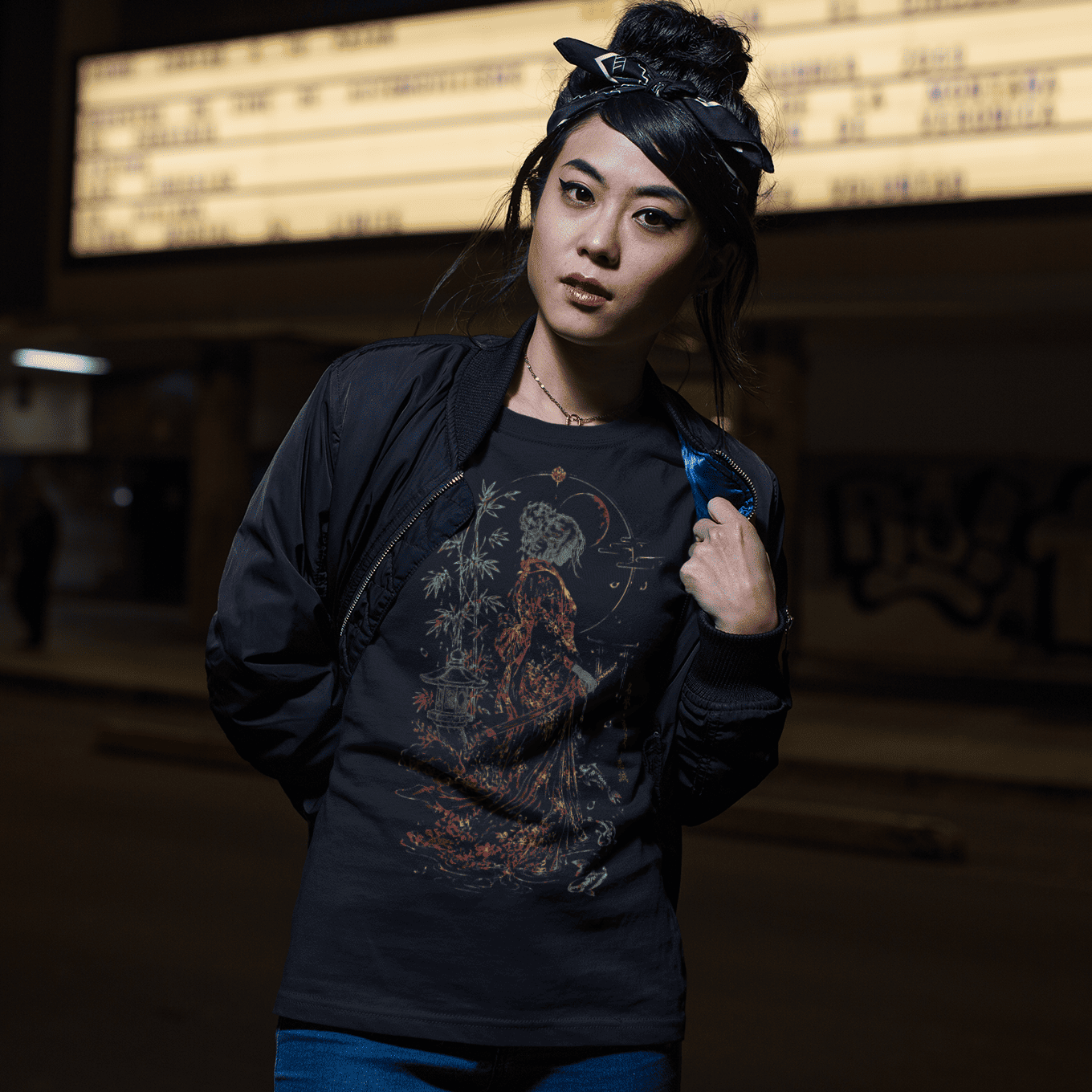Female model wearing Female Samurai T-Shirt with moonlit warrior artwork in a dark urban night setting.
