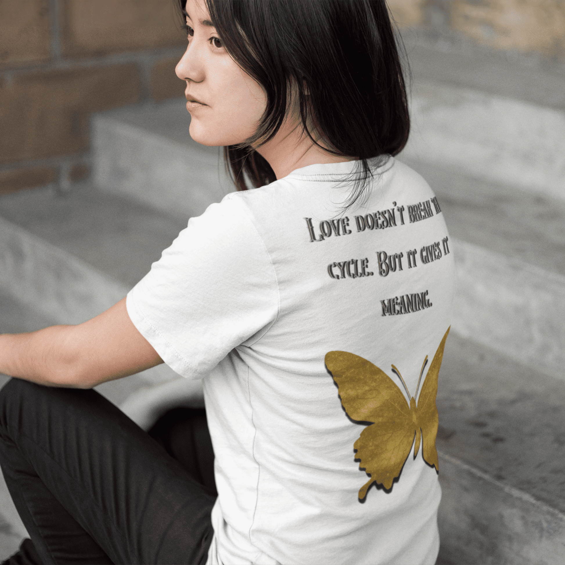 Person wearing a white t-shirt with a butterfly design and text on the back, sitting on steps.