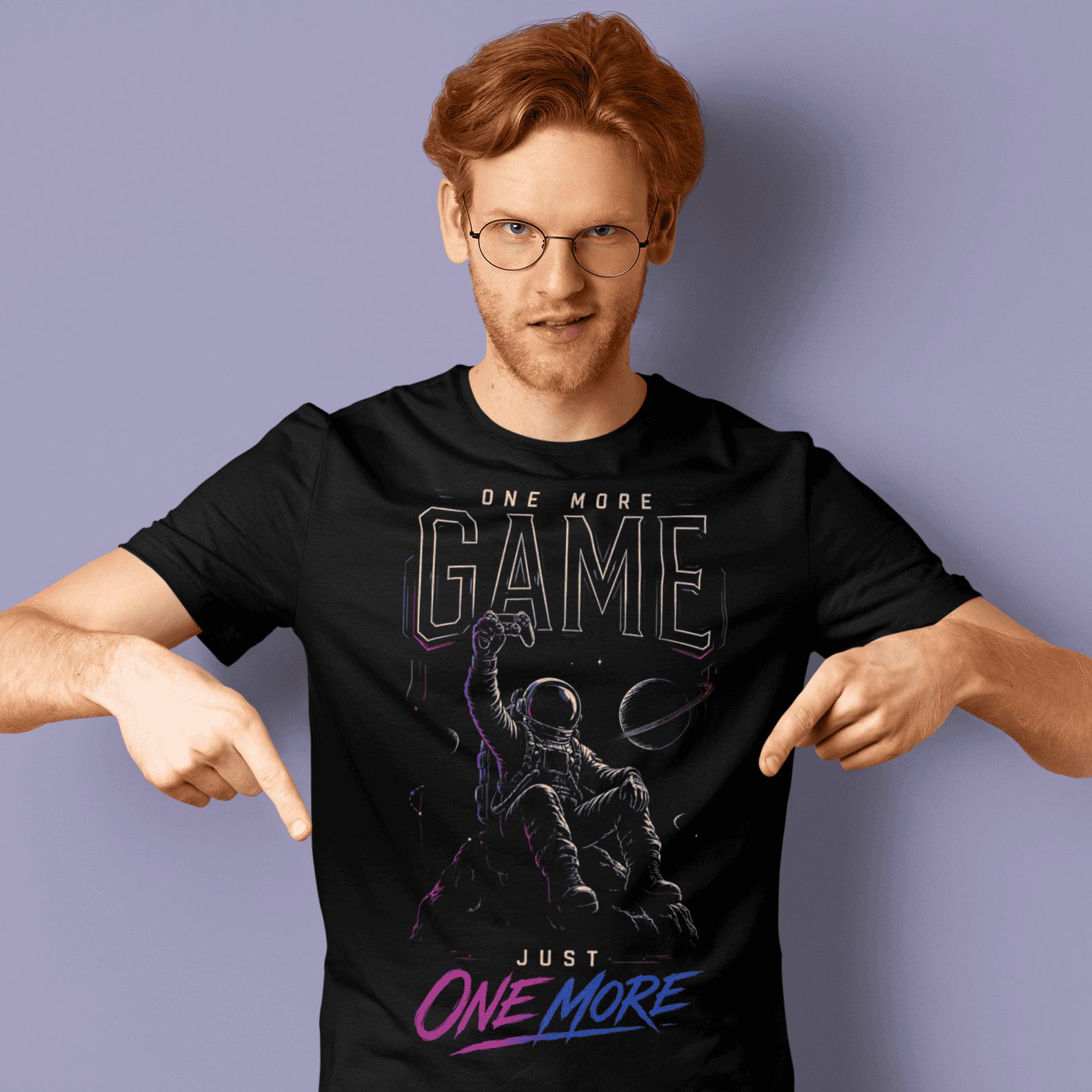 Male gamer pointing at One More Game T-shirt with dark gaming graphic on a purple studio background.