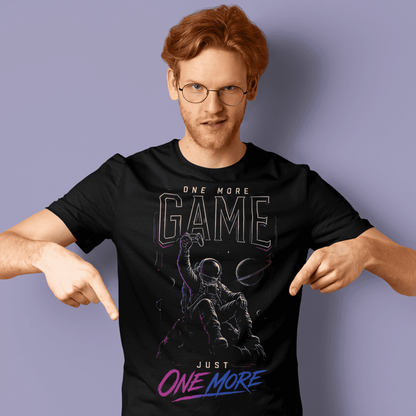 Male gamer pointing at One More Game T-shirt with dark gaming graphic on a purple studio background.
