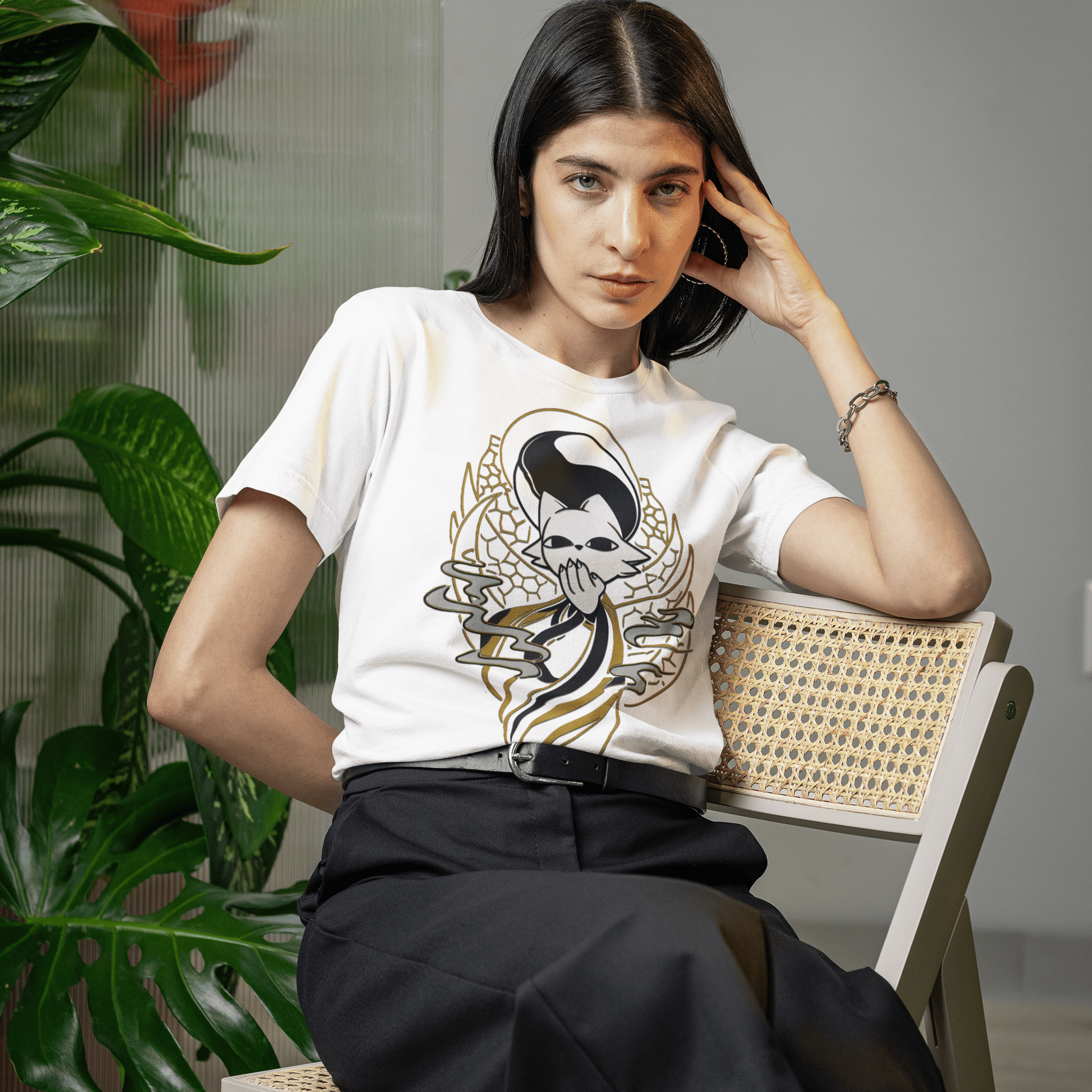 Female model sitting on a chair wearing the white Nine Sols Yin Yang Tee – Balance Presence beside tropical plants.