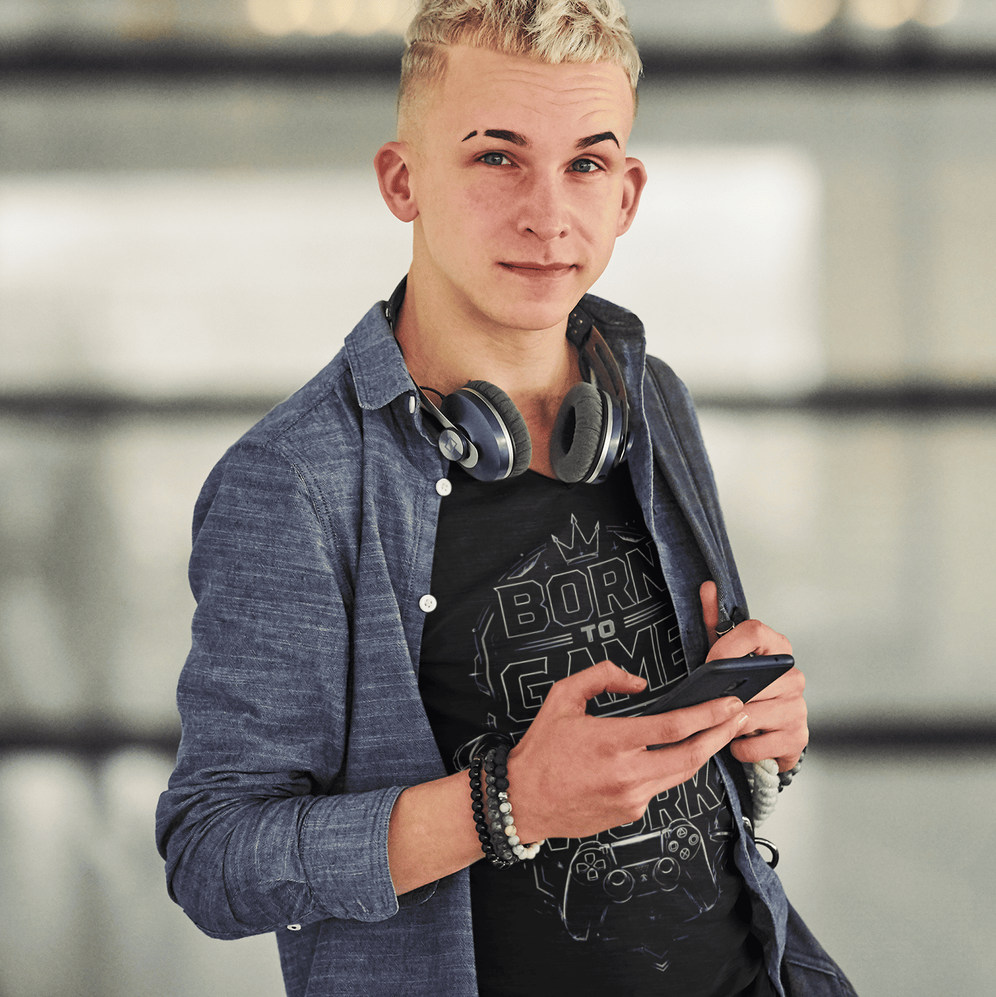 Front lifestyle view of Born to Game Forced to Work T-Shirt – Headset Gamer Mode worn by a model holding a phone