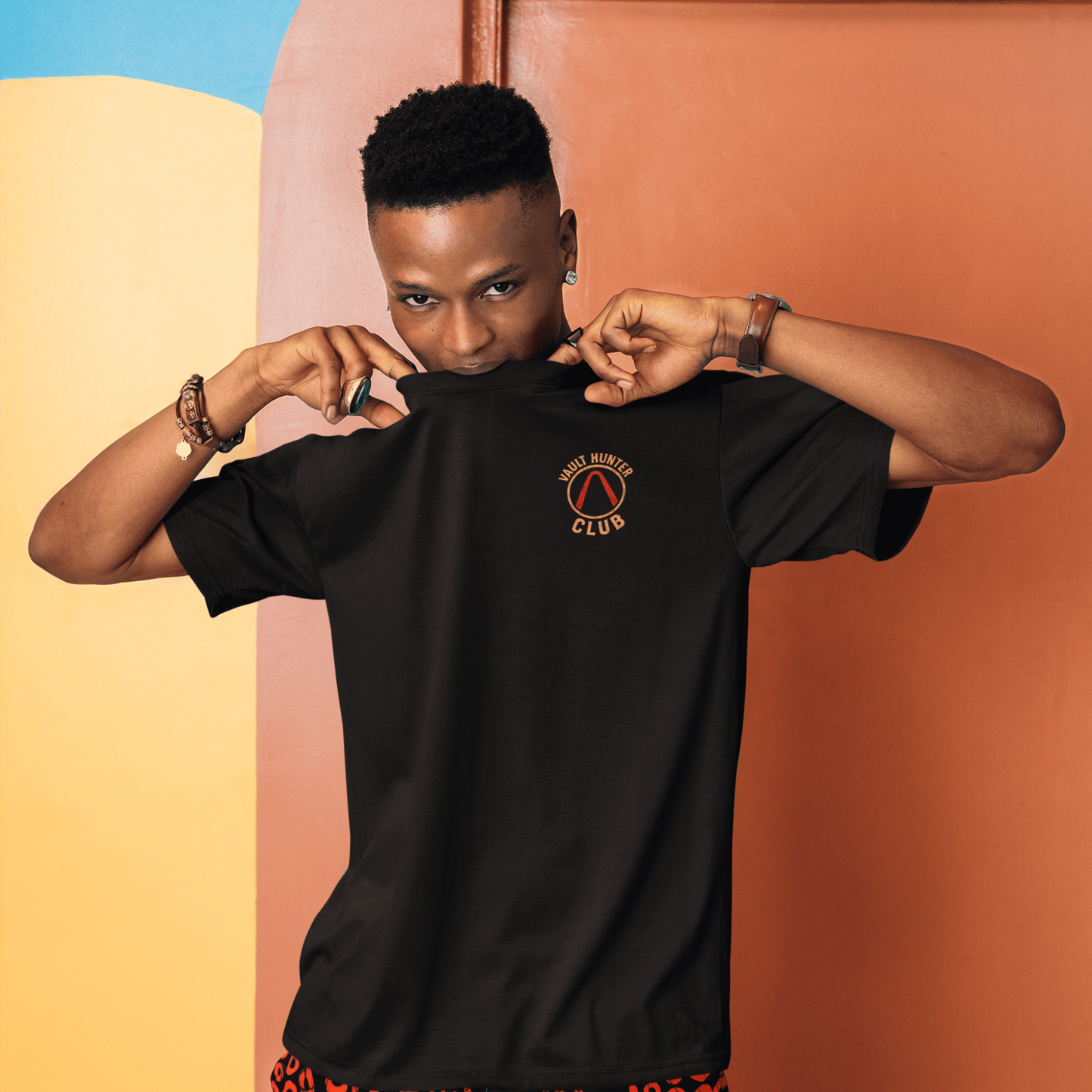 Person wearing a black t-shirt with a logo and colorful pants against a multicolored background