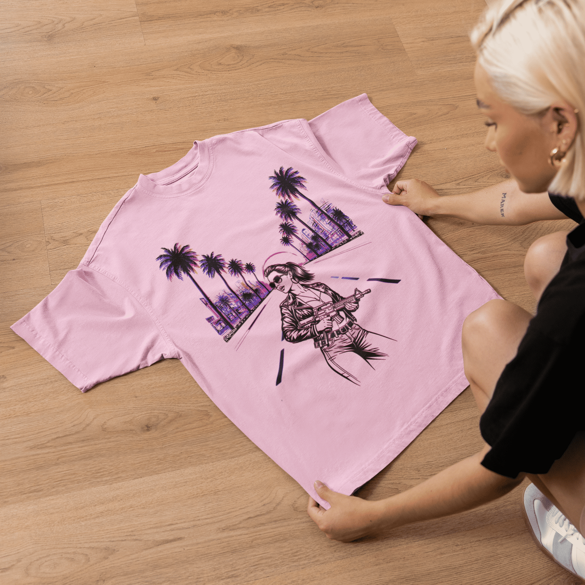 Person holding a pink t-shirt with a graphic design on a wooden floor