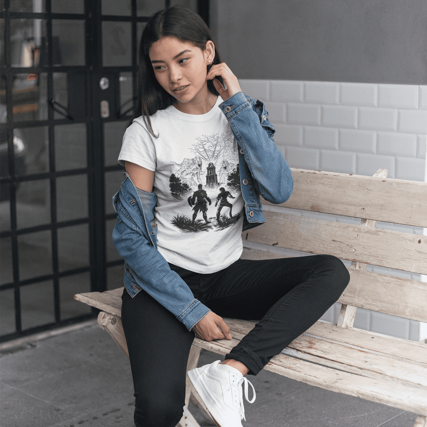 Woman sitting on a bench wearing a graphic t-shirt, black pants, and white sneakers.