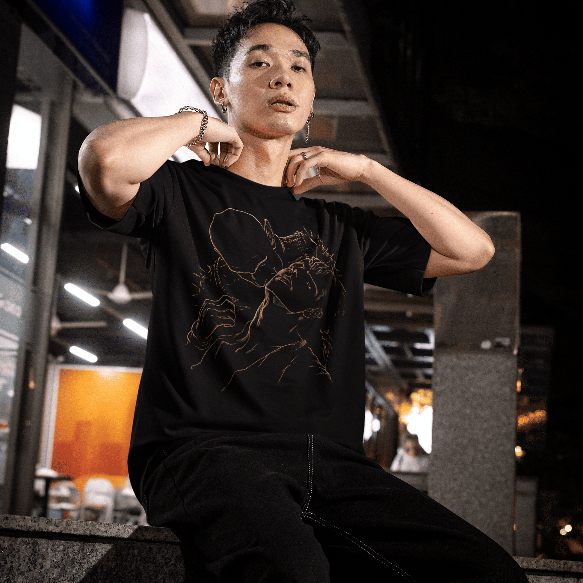 Seated night model view of The Blood of Dawnwalker Sire Embrace T-Shirt with subtle gold vampire design.