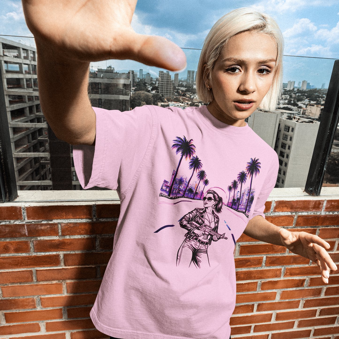 Person wearing a pink t-shirt with a graphic design on a rooftop with cityscape background