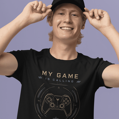 Front view of My Game Is Calling T-Shirt – I Must Go Gamer Mood worn by a smiling model adjusting a black cap