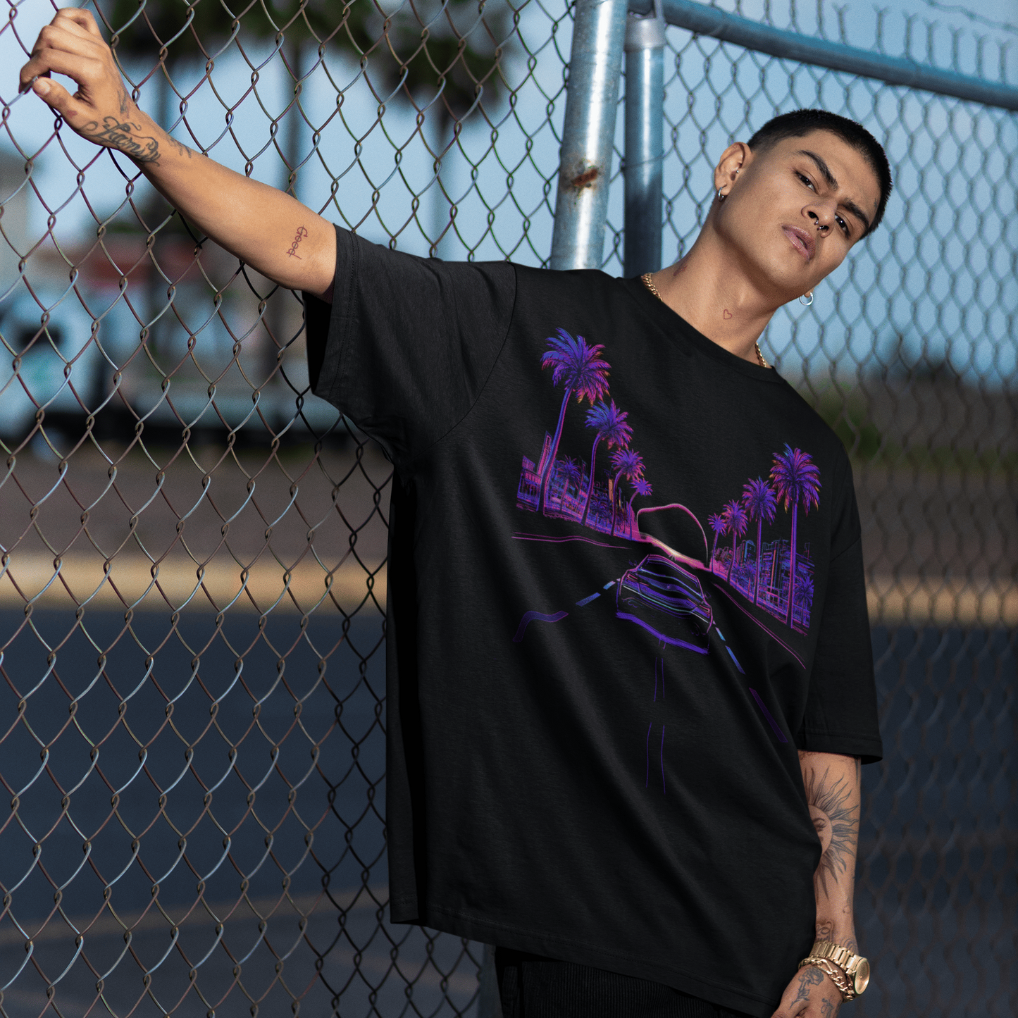 Person wearing a black t-shirt with a purple graphic design, leaning against a chain-link fence.