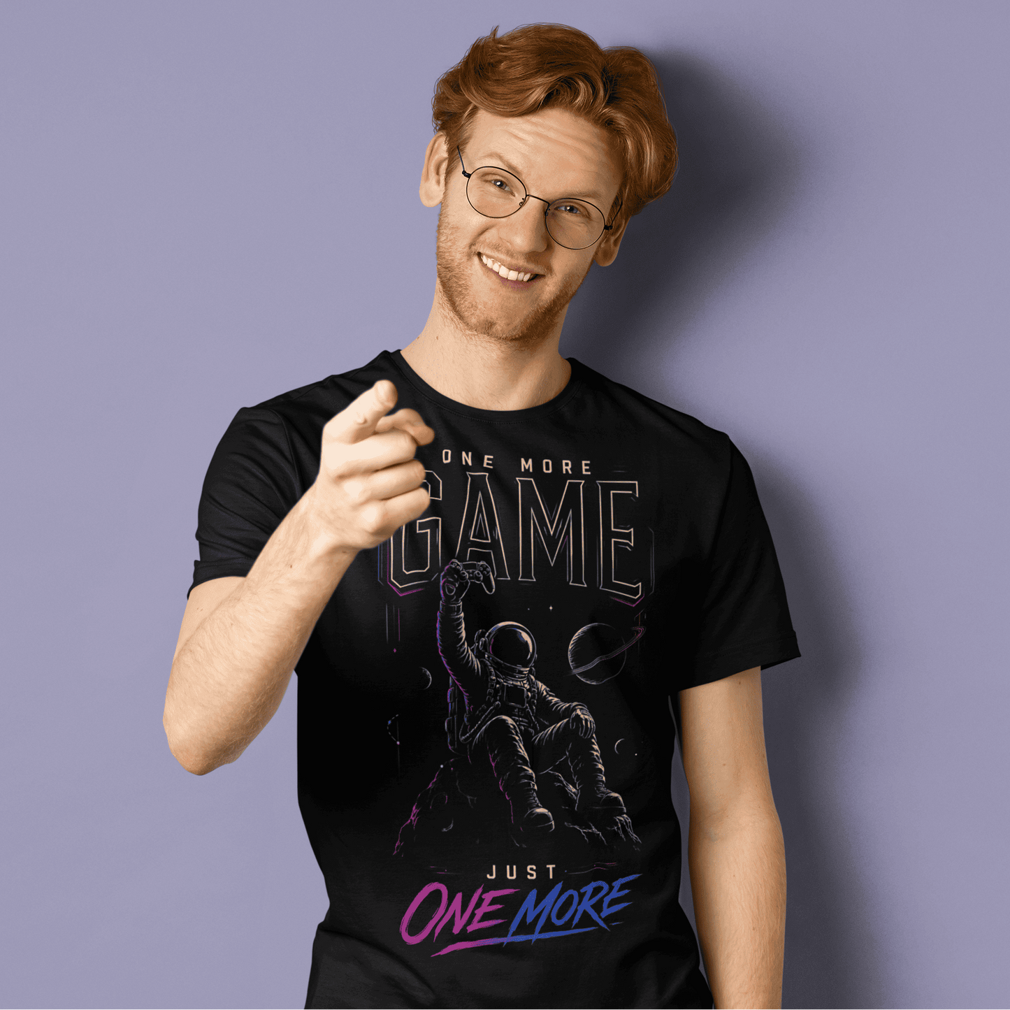 Smiling male gamer giving a thumbs-up in One More Game T-shirt with dark gamer graphic on purple background.