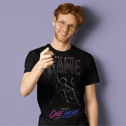 Smiling male gamer giving a thumbs-up in One More Game T-shirt with dark gamer graphic on purple background.