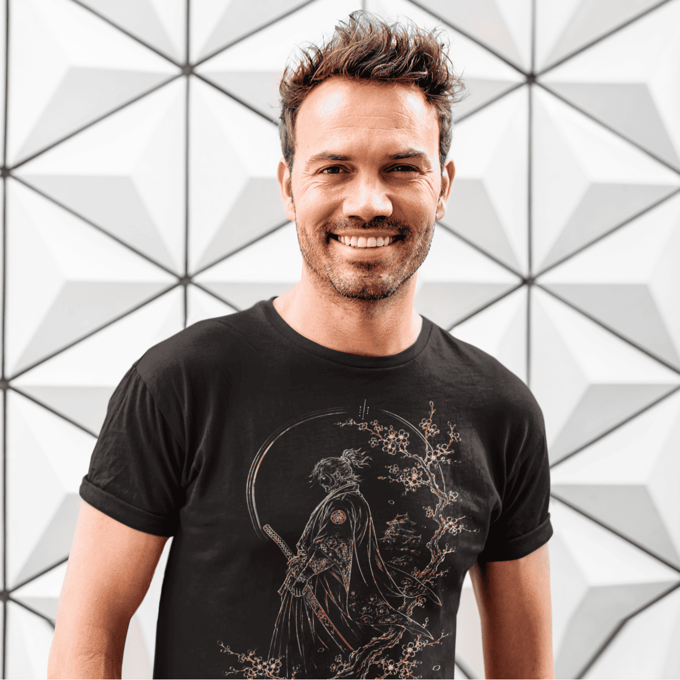 Smiling male model wearing Lone Samurai T-Shirt with cherry blossom warrior artwork against a white geometric wall.