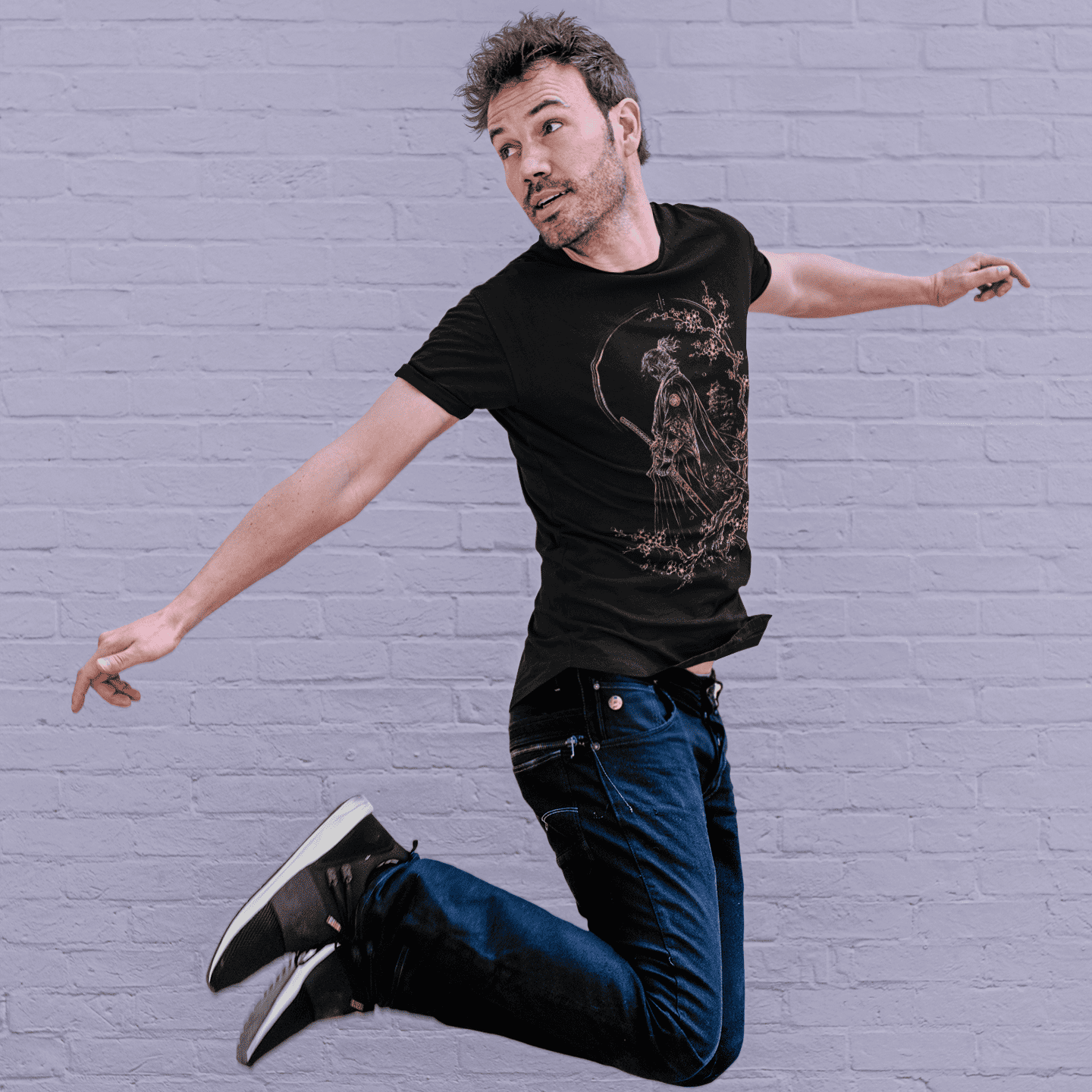 Male model jumping in Lone Samurai T-Shirt with samurai artwork and cherry blossom details on a purple background.