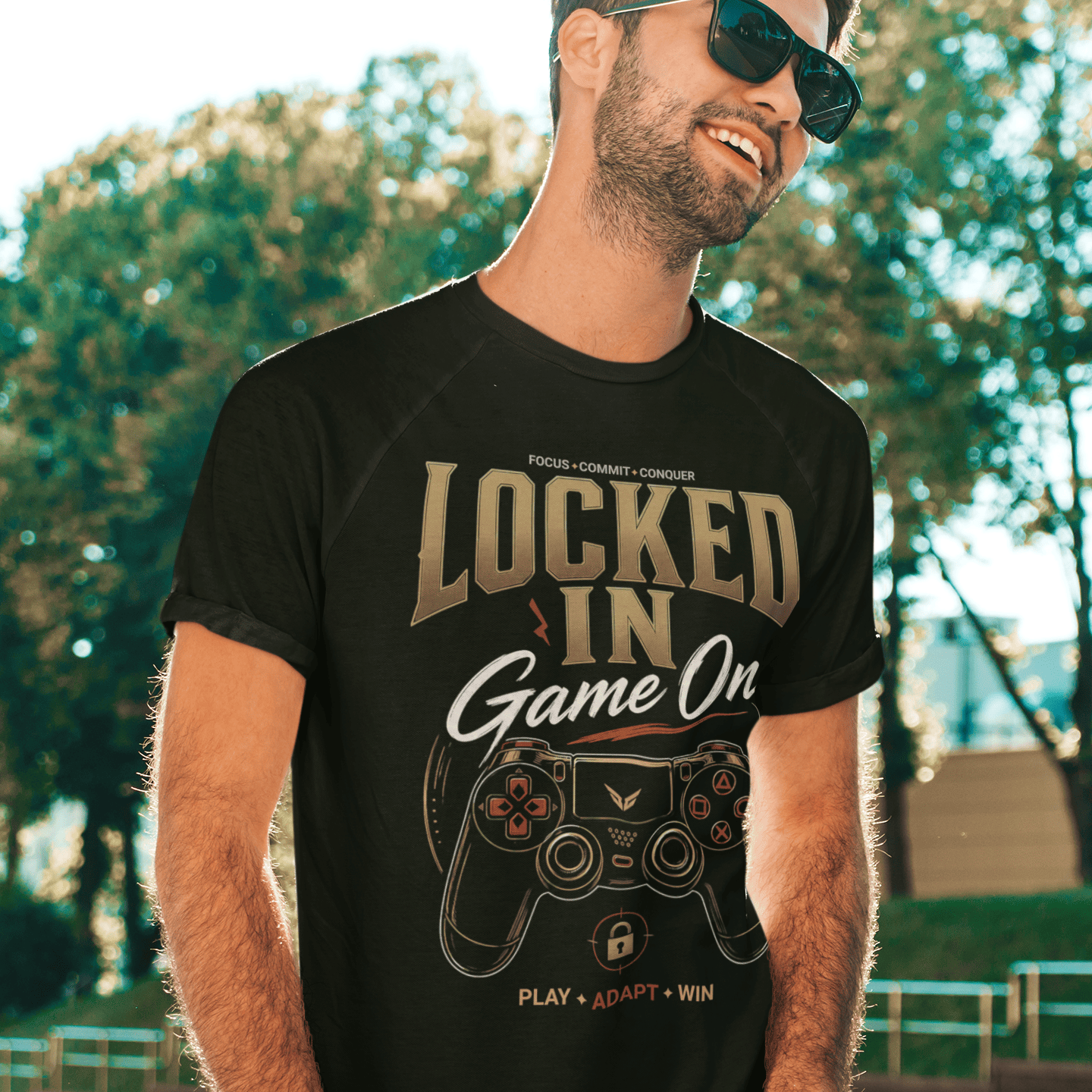 Male gamer posing in Locked In Gamer T-Shirt with focused gaming artwork against a sunlit urban background.