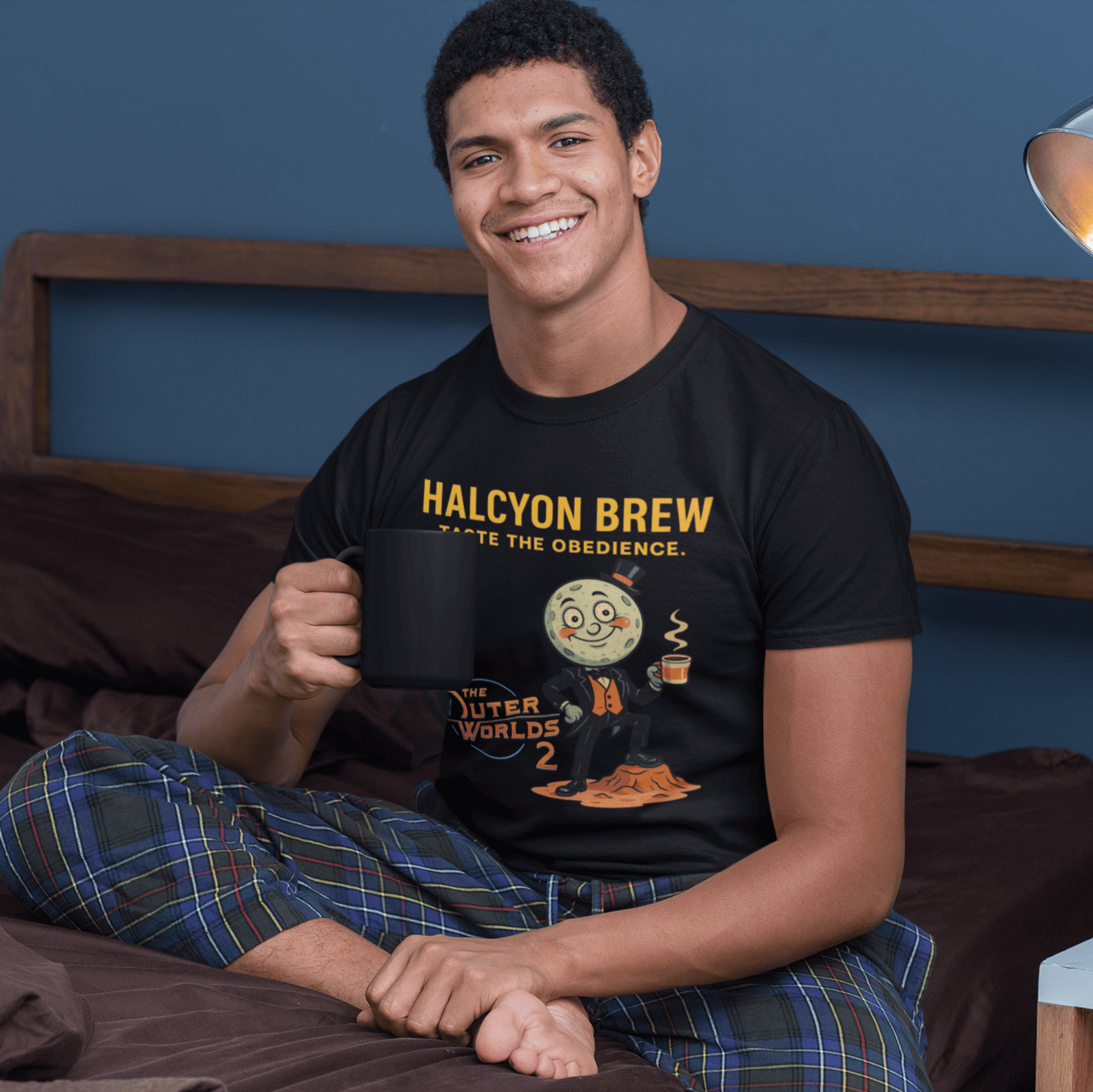 Person wearing a black t-shirt with 'Halcyon Brew' design, sitting on a bed holding a mug.