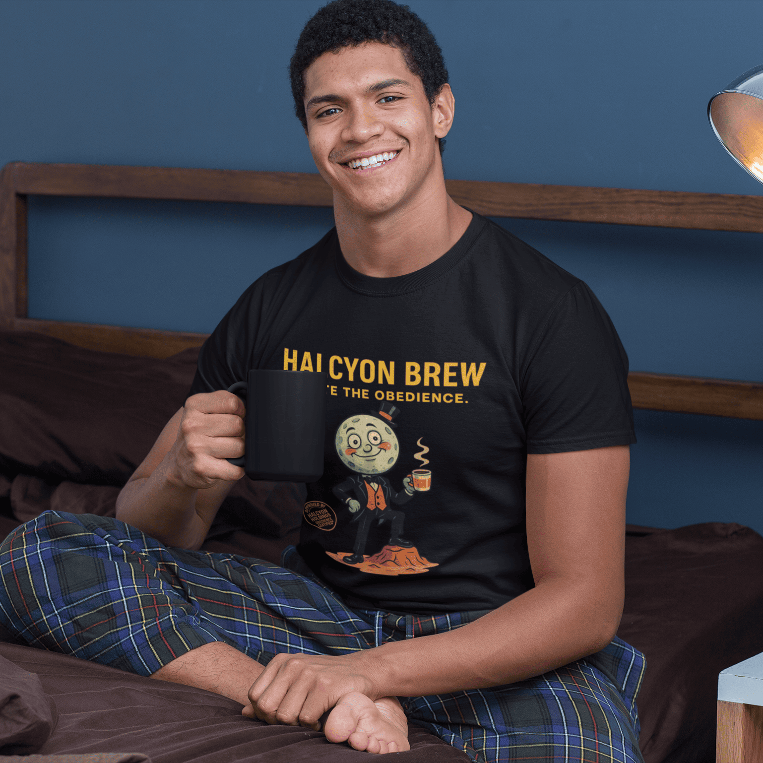 Model wearing The black Outer Worlds 2 Halcyon Brew T-Shirt showing front print while sitting on a bed with a mug