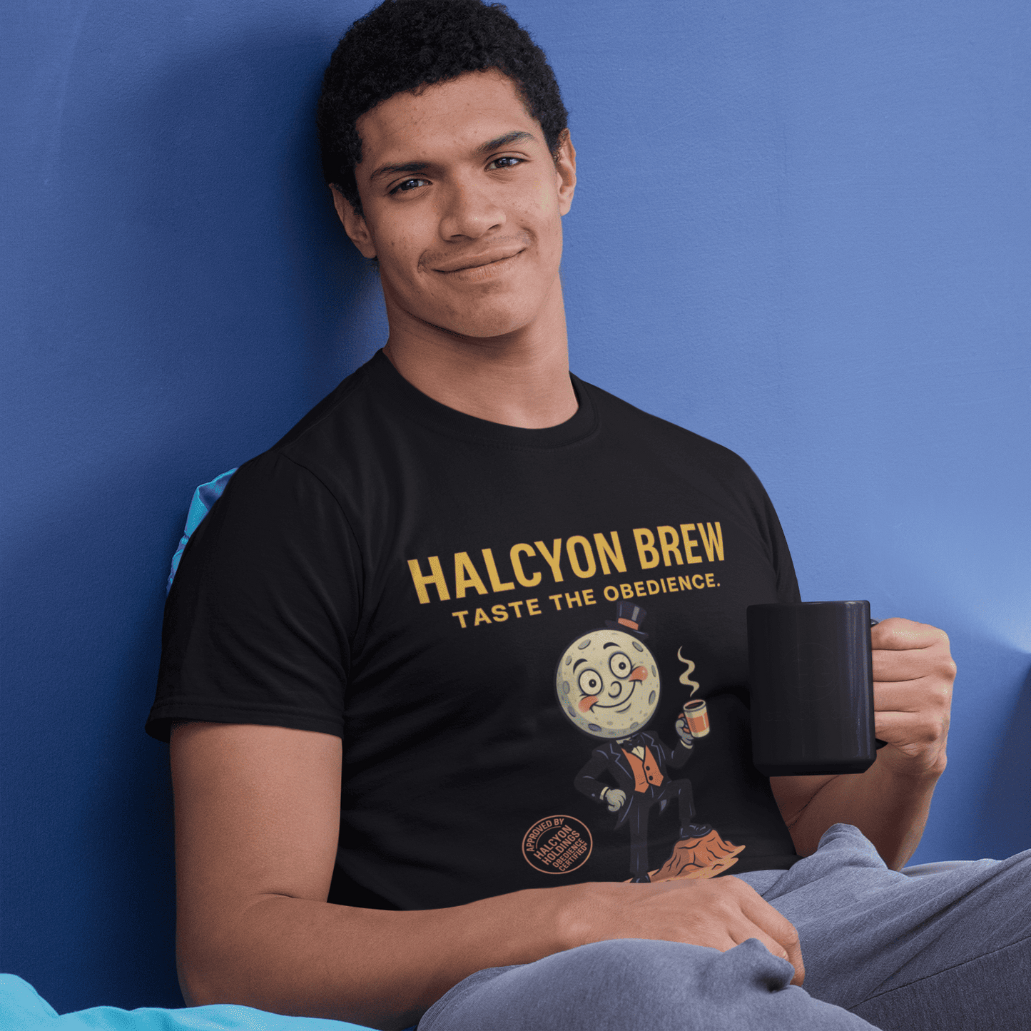 Model wearing The black Outer Worlds 2 Halcyon Brew T-Shirt showing front artwork while seated against a blue wall