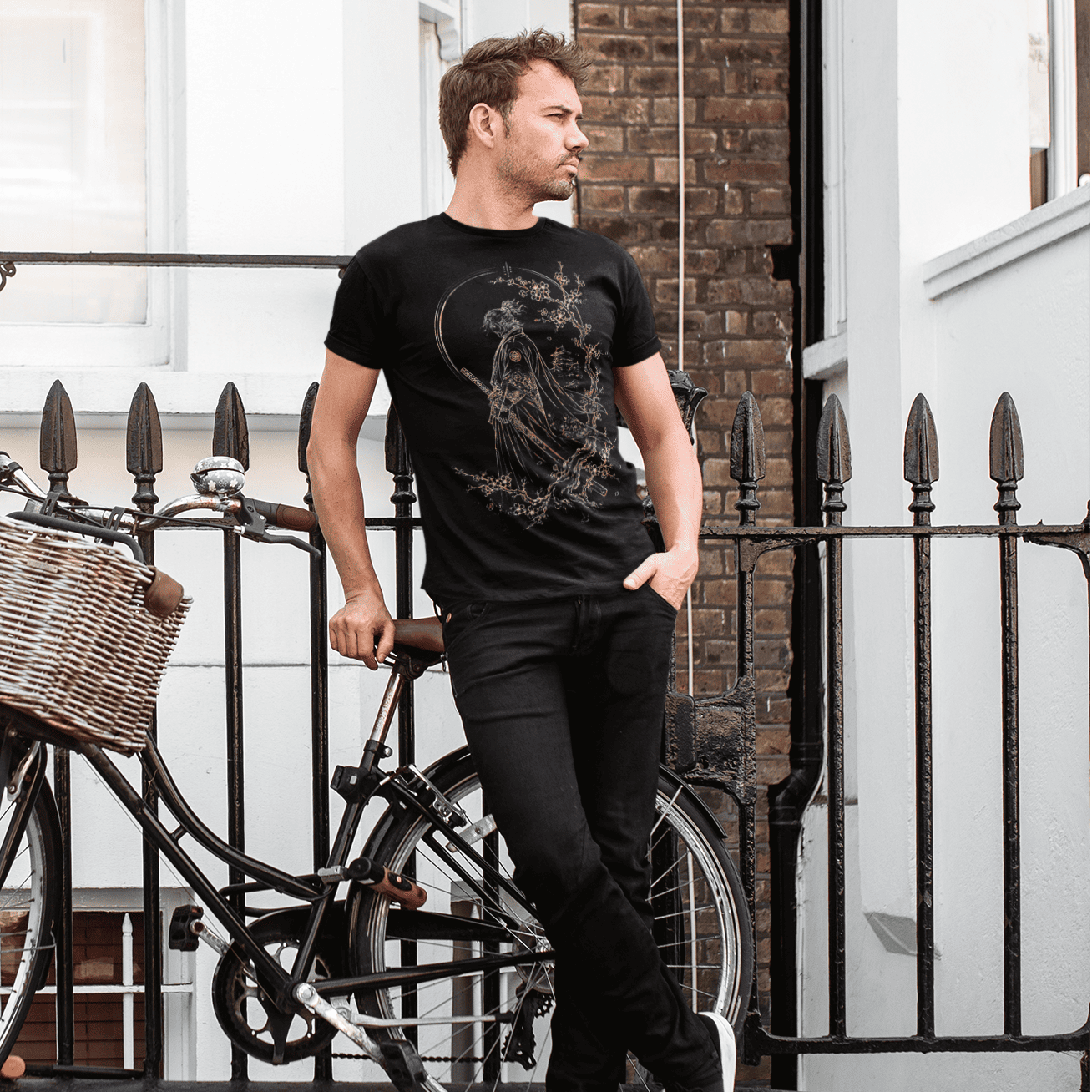 Male model wearing Lone Samurai T-Shirt with warrior artwork on a city street beside a bicycle.