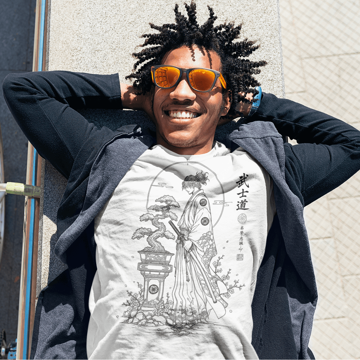 Close-up of smiling male model in Bonsai Samurai T-Shirt with Bushido warrior artwork beside a white brick wall.