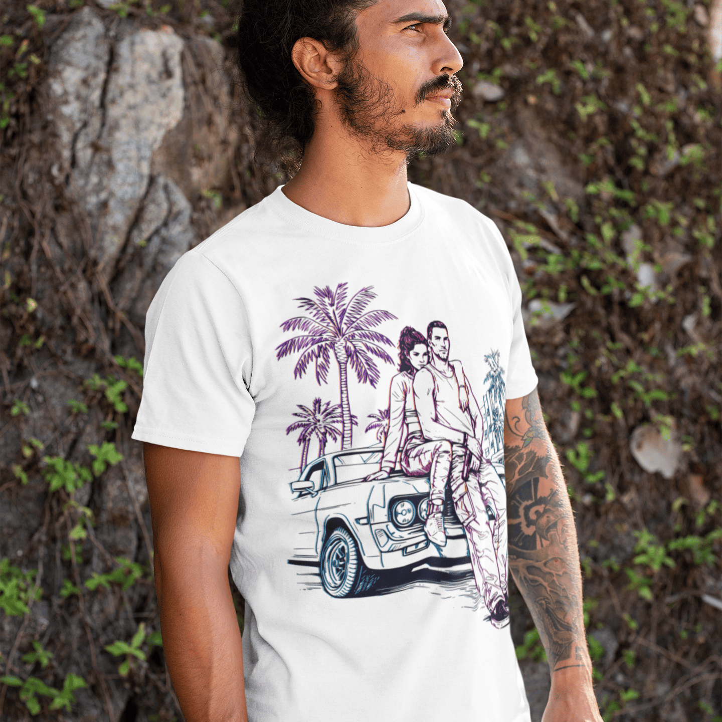 Man wearing a white t-shirt with a graphic design of a car and palm trees, standing against a natural background.