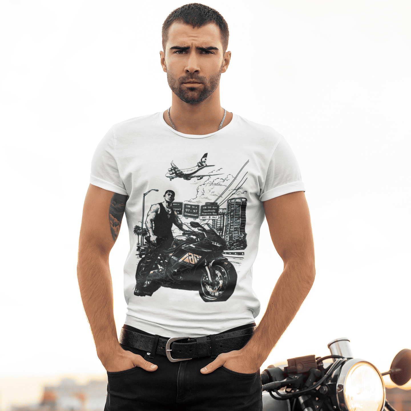 Man wearing a white t-shirt with a graphic design, standing next to a motorcycle.